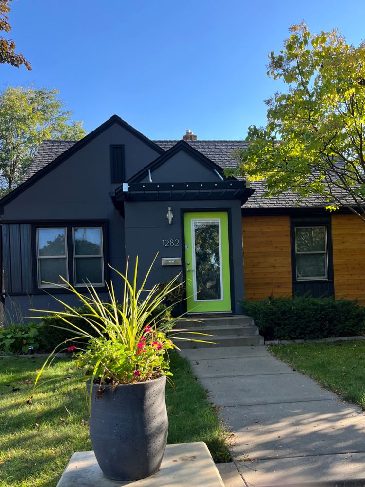 House with dark gray paint, lime green door, and wood paneling. Planted in foreground