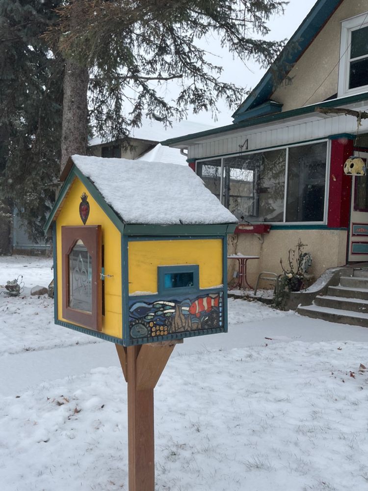 Yellow little free library covered with snow. One side has an underwater mosaic scene