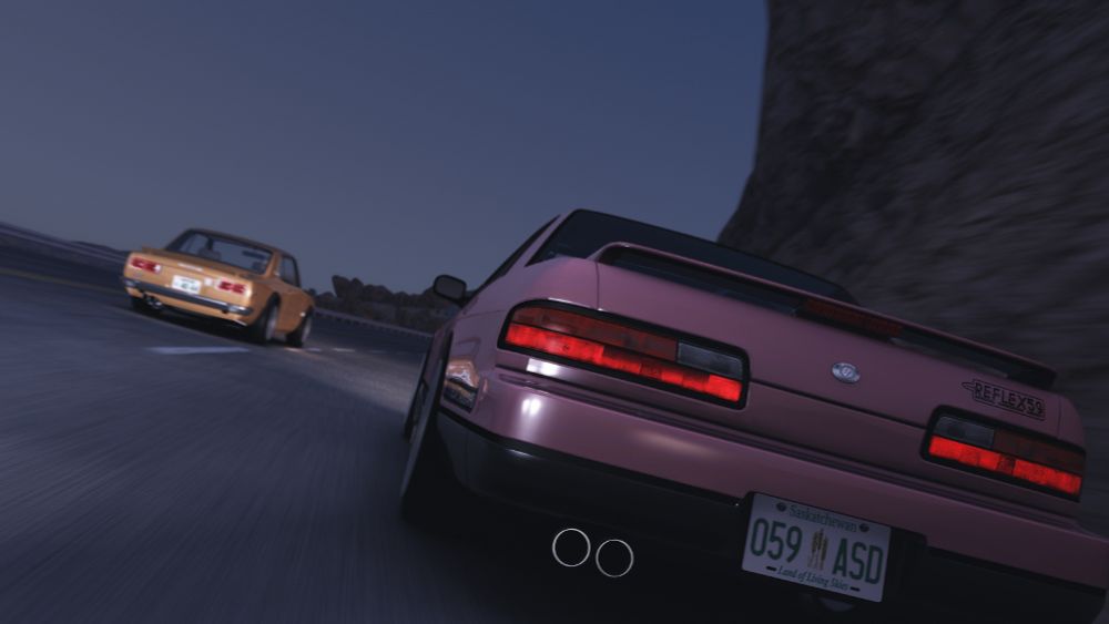 A pink Nissan Silvia S13 and a Nissan Skyline C10 racing down a cliffside highway at dusk.