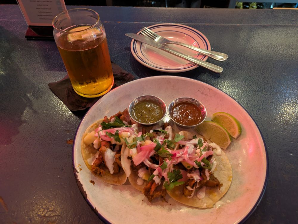 A glass of beer next to a delicious plate of tacos 
