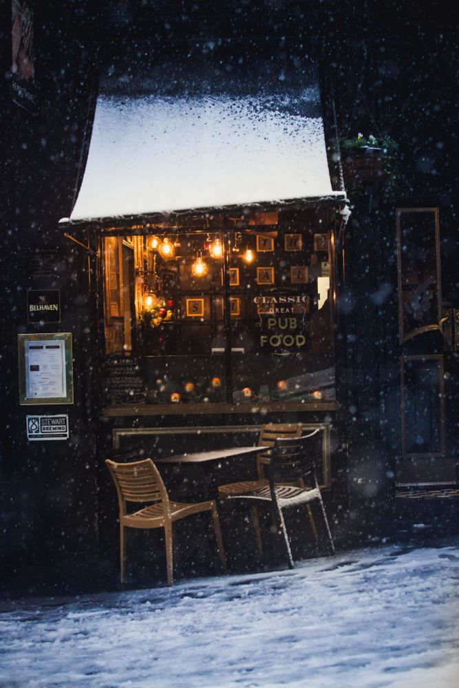 Snow falling outside a warmly lit pub