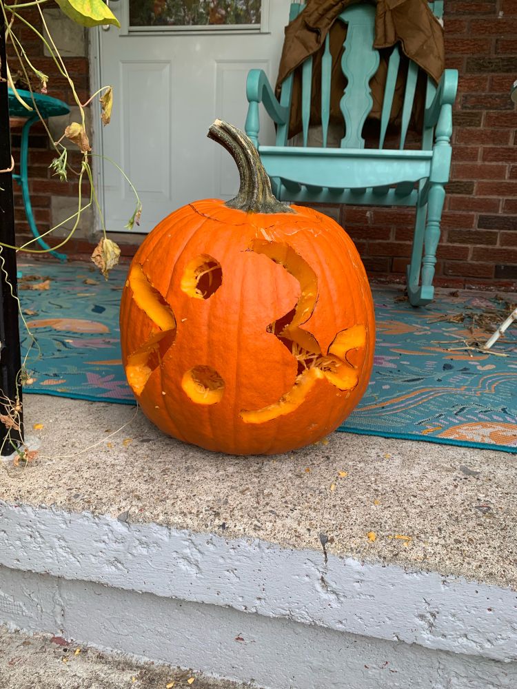A jack-o-lantern carved to look like a mischievous cat face emoticon. The jack-o-lantern is not lit and the photo is shot during the day.