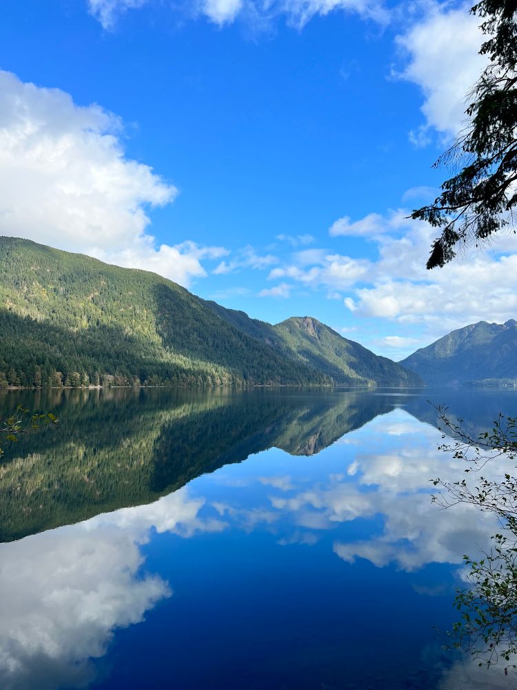 A photo of Lake Cresent in Olympic National Park, on a sunny day with the mountains clearly reflecting in the water. 