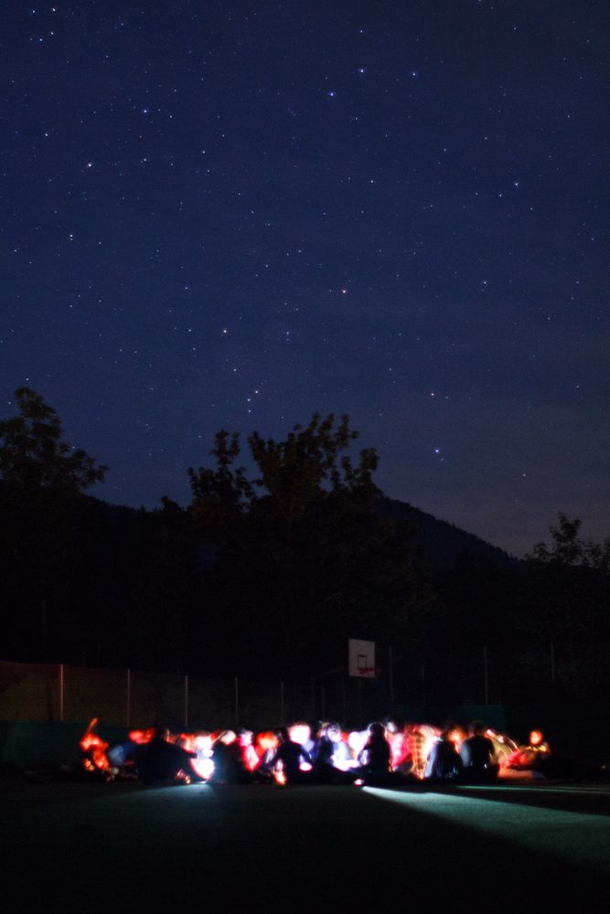 Image: campers reading with flashlights under a starry sky 