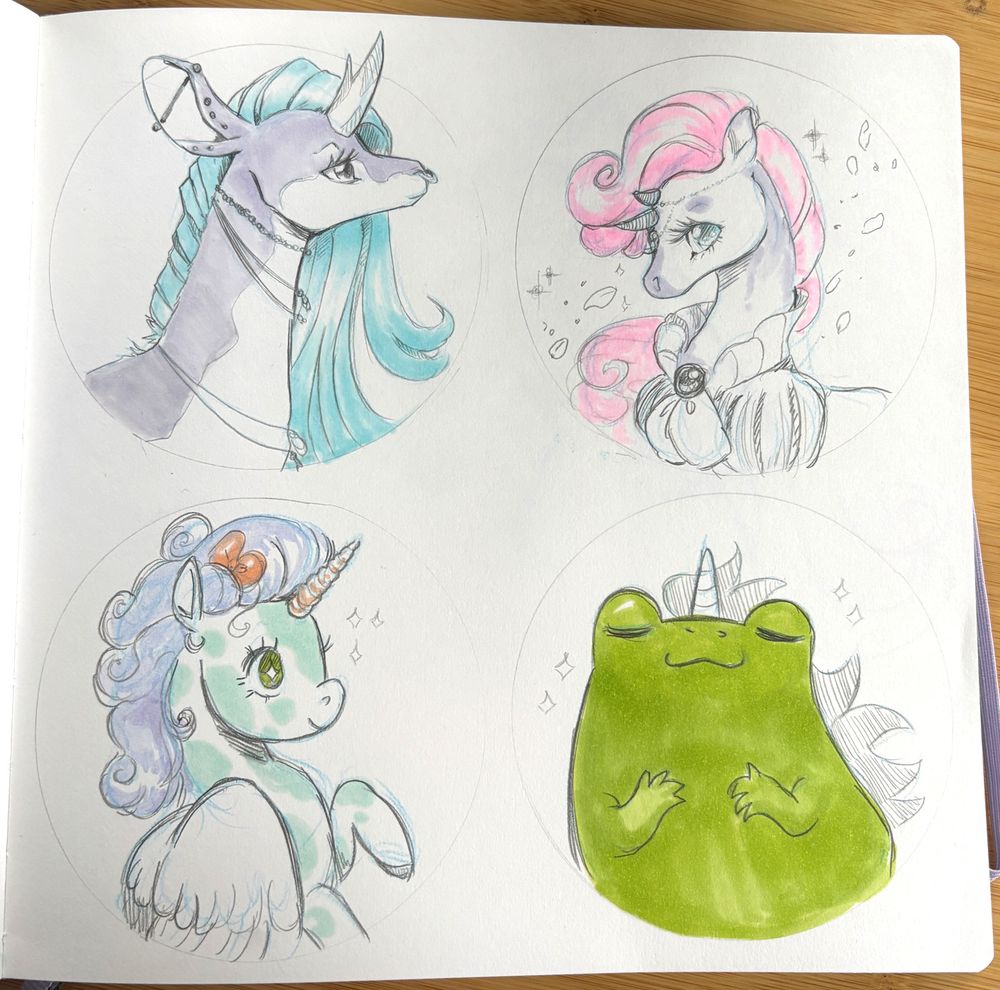 Photo of sketchbook page showing four unicorns. Top left; unicorn with two spiked horn, large peirced ears, necklaces and long blue hair. Top right; princely unicorn with sparkling sad eyes and pink hair, wearing a puffy sleeved top. Bottom left; happy sparky eyed unicorn with green spotted body and purple fauxhawk hair and white wings. Bottom right; a frog with a happy face, unicorn horn and flowing mane. 