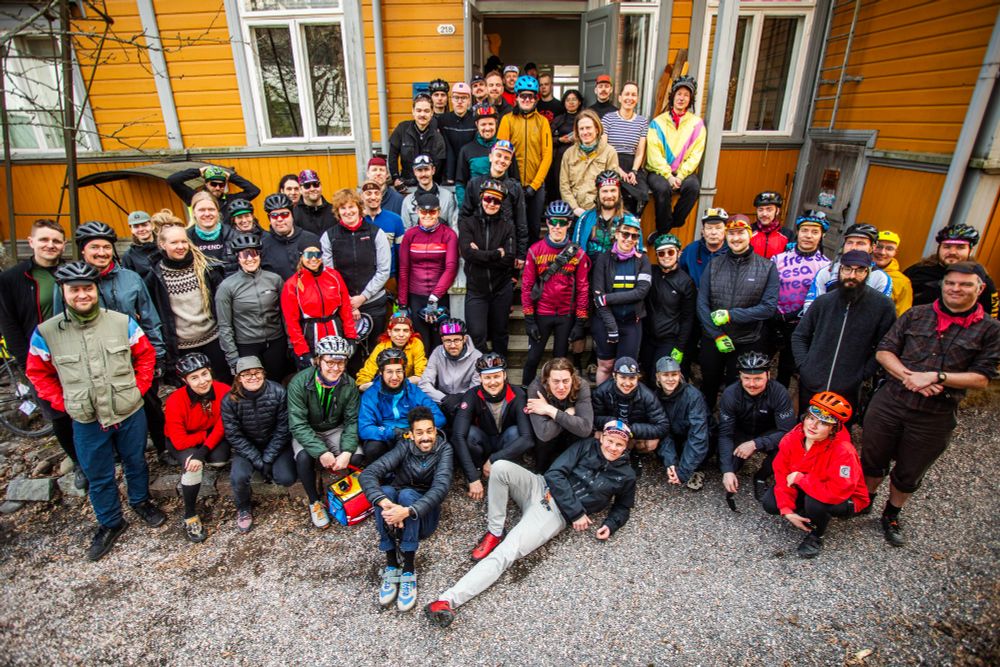 Suuri joukko pyöräilijöitä ryhmäkuvadsa Kaisan ja Lekan kuistilla ja kuistin vieressä. 