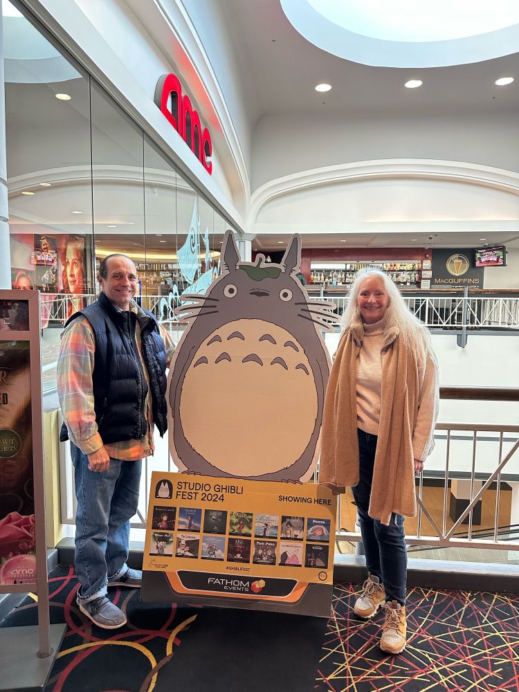 Two people standing next to a life-size cardboard cutout of Totoro at the movie theater 