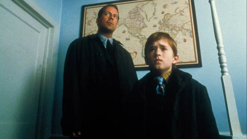 A man in an overcoat stands behind a little boy in a blue room. There is a framed map behind them.

(Image is of Bruce Willis and Haley Joel Osment in THE SIXTH SENSE.)