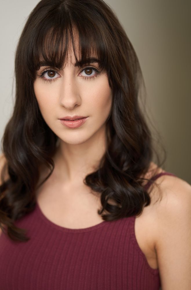 A young woman in a burgundy top looks into the camera, her dark hair falling past her shoulders.