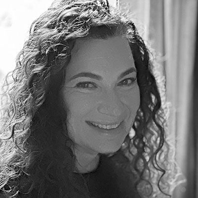 A black-and-white close-up of a woman smiling for the camera. The sun plays through her hair from the window behind her.