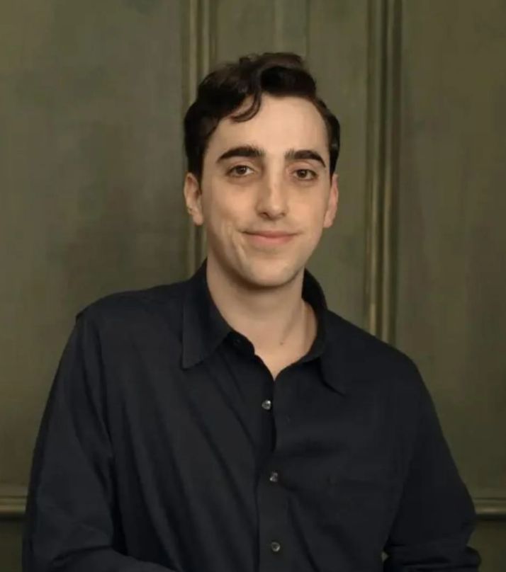 A young man wearing a black dress shirt smiles for the camera.
