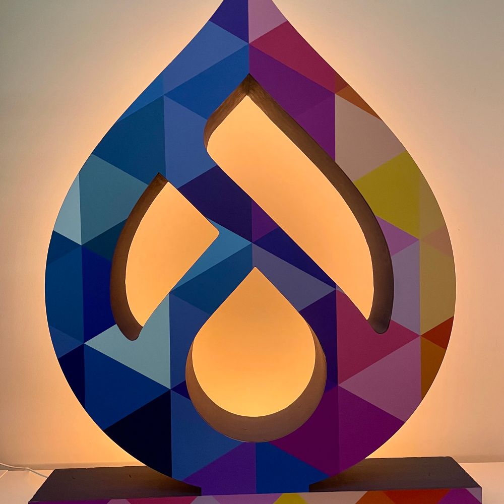 Background lit colourful Drupal Europe drop-shaped logo panel in front of a white wall