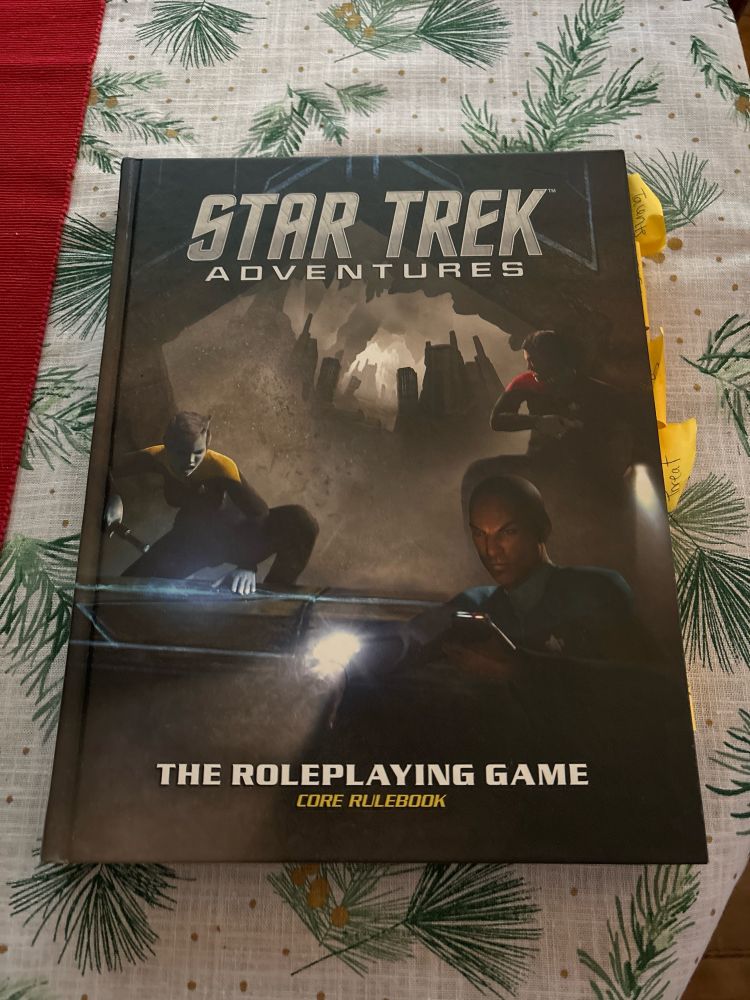 The core rulebook for Star Trek Adventures on a table with a wintery white and green tablecloth background. 