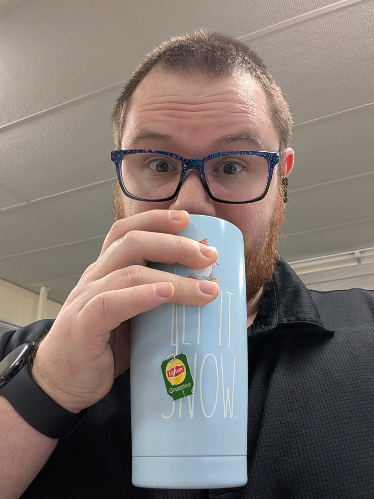 Me, a human male, drinking green tea out of a blue tumbler with the words let it snow on the side. My fingers covered up the cute penguin by accident. 