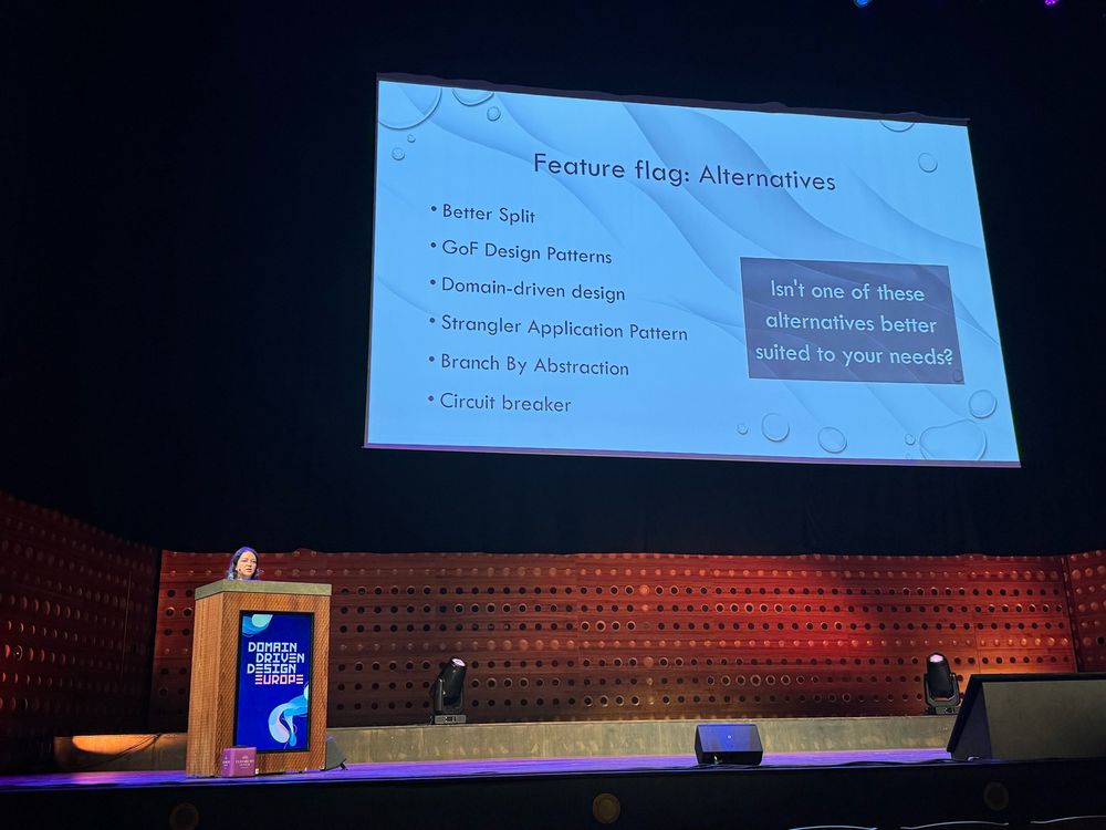 Dorra on stage with the screen recapitulating alternatives to feature flags