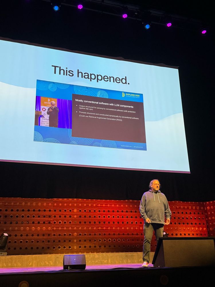 Tobias standing on stage in front the screen showing the picture of Eric Evan’s talk at last year DDD Europe 
