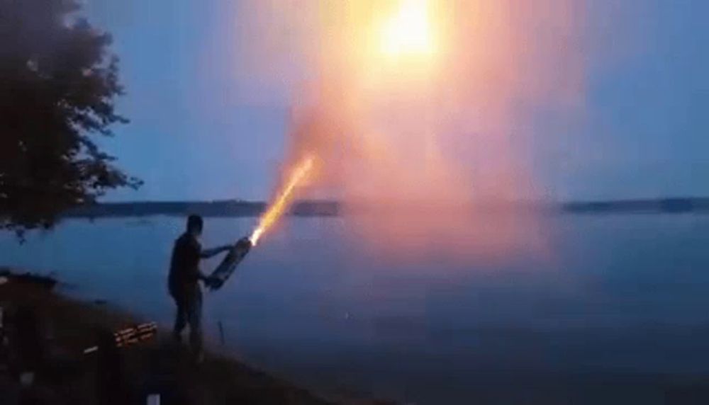 a man is holding a torch in front of a lake at sunset .