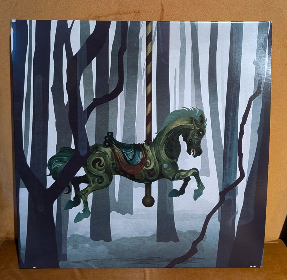 A photo of a vinyl album cover showing a drawing of a Merry-Go-Round horse prancing in a dark, misty leafless forest 