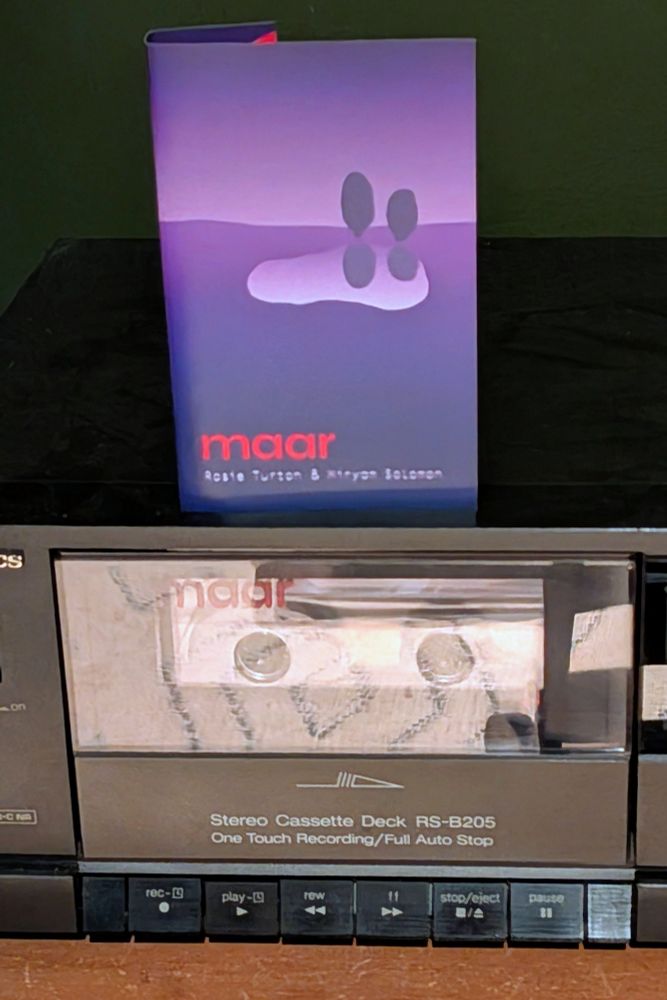 A tape on top of a cassette deck. The tapes artwork shows two different waves of purple and a lilac island with two black shapes on it