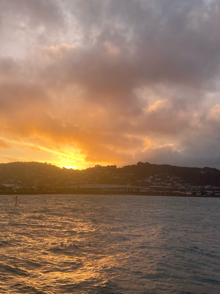 Sun setting behind hills in the distance, it’s light reflecting over an Ocean Bay. 