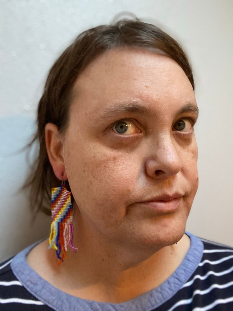 A woman wearing beaded earrings, with colors from lesbian and pride flags. 