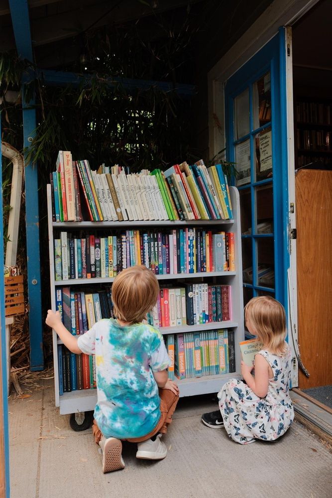 Two children are looking at a bookshelf filled with various colorful books.