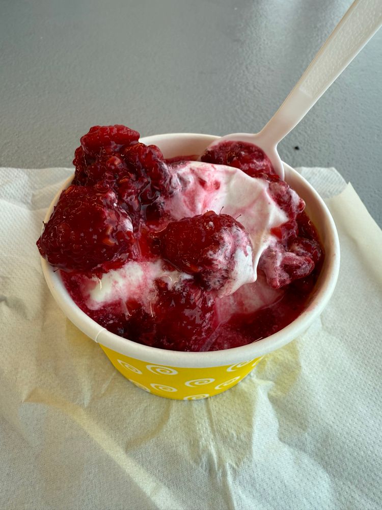 Raspberry sundae made with lactose-free vanilla soft serve. Yellow cup and spoon.