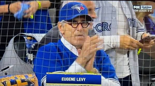 Eugene Levy at Game 6 wearing a Blue Jays hat and clapping for the home team