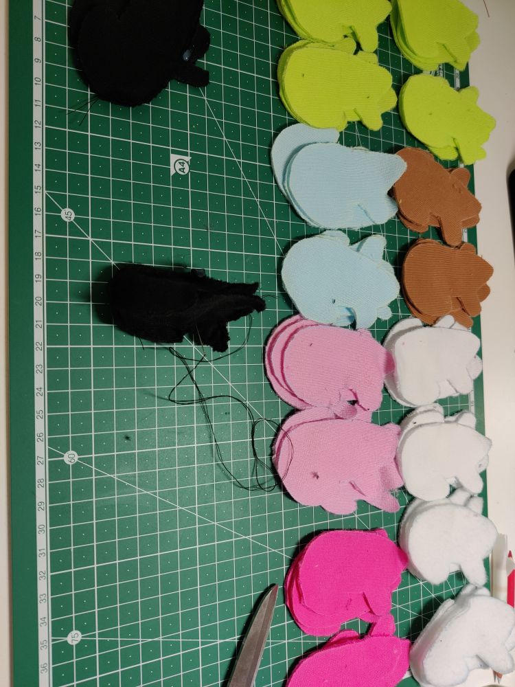Many pieces of fabric cut to make small frog plushies, laid out on a cutting mat.