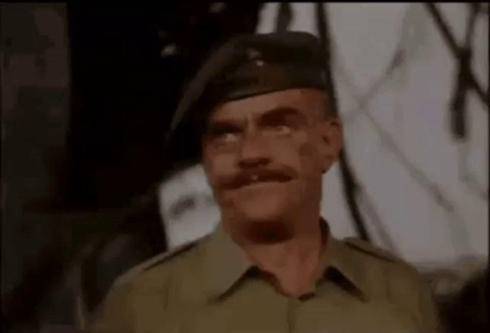 a man in a military uniform with a mustache is wearing a beret and making a funny face .