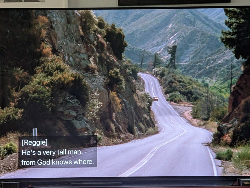 A car driving down a long stretch of highway. On the screen are the words: He's a very tall man from God knows where. 
