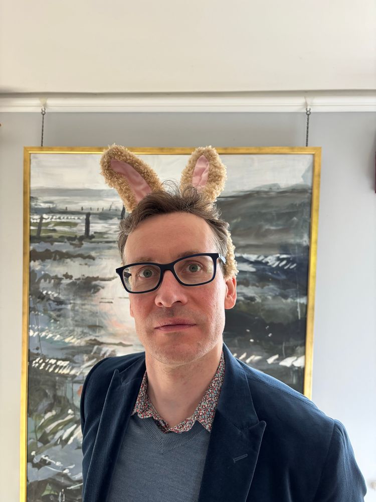 Richard Elwes wearing bunny ears in front of a painting.