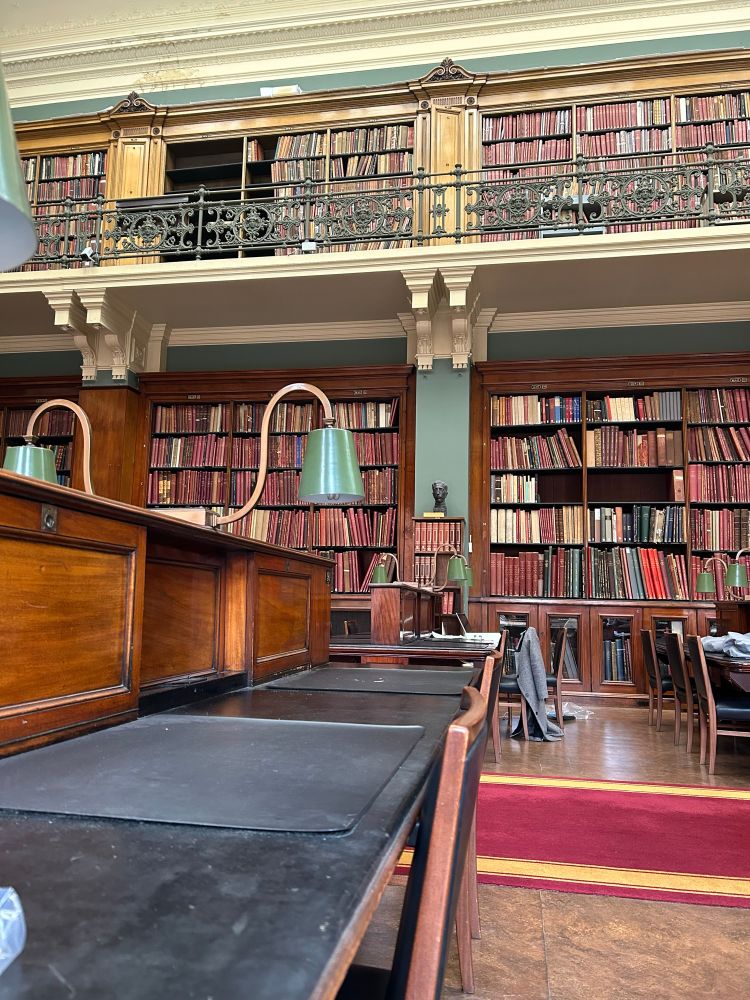 The national art library- gorgeous old wooden shelves, a balcony with more shelves, and old leather bound books on them in dusty reds and pinks and oranges