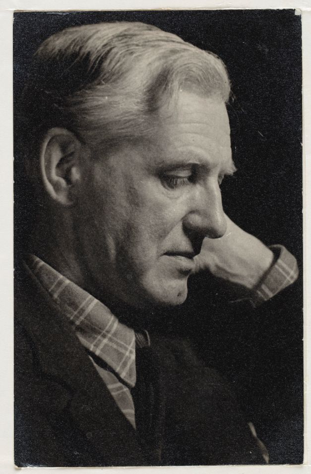 A black and white photo of Kingsley Read, the designer of the Shavian alphabet, taken in 1947. He has grey hair and looks down pensively. The lighting is dramatic with a black background.