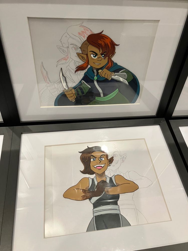 A photo of two 11 x 14” matted frames, each with a mock anime cel inside, backed by a relevant douga/pencil drawing. This one features Rollo, a halfling brandishing two daggers, and Piper, a wolfy half-elf monk.