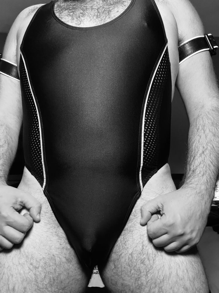 A monochrome photo of a torso in an athletic bodysuit. Both biceps have leather arm bands around them.