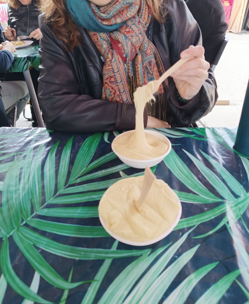 Adl levant sa fourchette dans son bol d'aligot pour me montrer les fils qu'il fait, mon bol devant elle, posé sur une table recouverte d'une nappe à motif de feuilles 