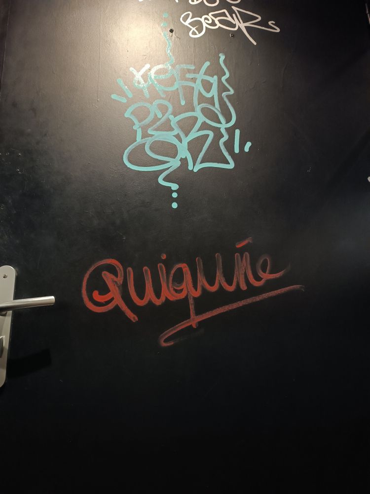 "quiquine" écrit en rouge sur la porte de toilettes de bar