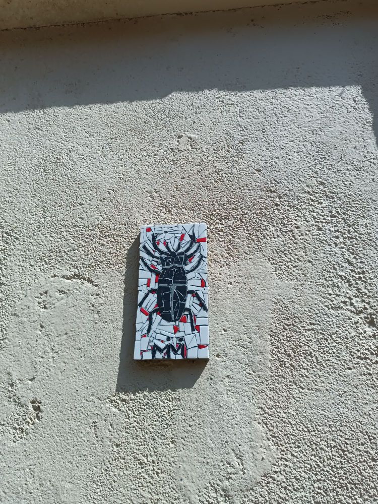 Mosaïque rectangulaire d'un insecte ressemblant à un scarabée à cornes posée sur un mur dans la rue au soleil