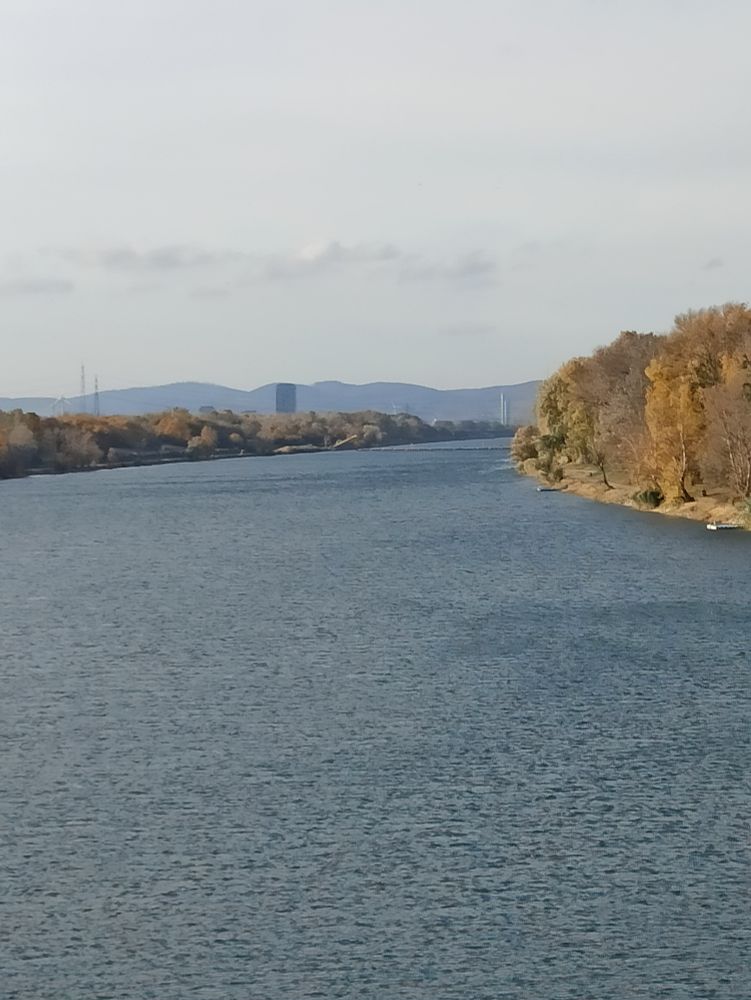 Wasserfläche am Ufer gelbfarbige Bäume im Hintergrund eine Hügelkette mit einigen Türme davor