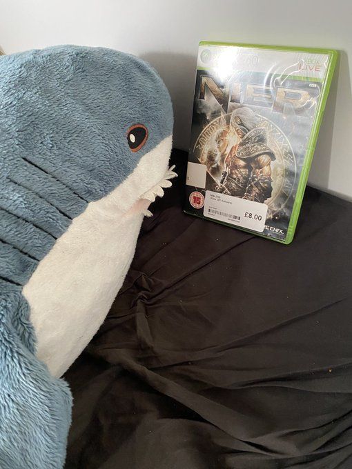 Shark plush looking at a copy of NieR for the Xbox 360