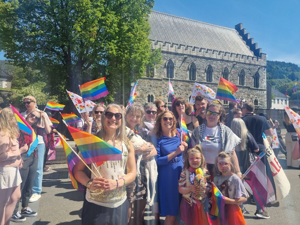Happy people with Pride flags in front of tall trees and an old building 
