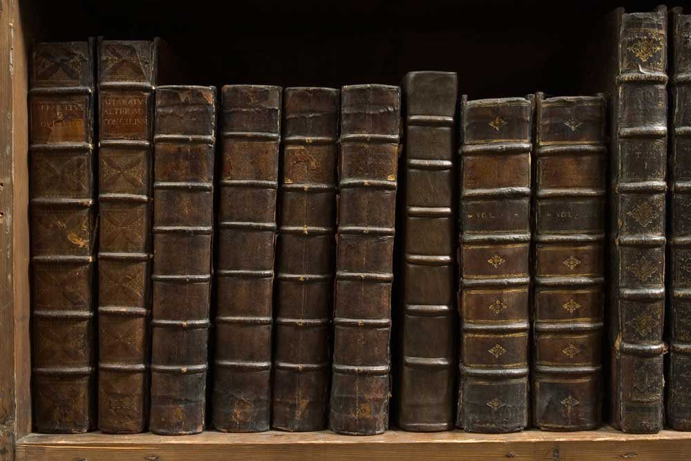 A bookshelf with a row of historic books, all bound in dark brown leather