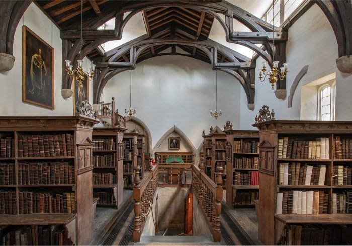 A photograph of the historic library at Westminster Abbey. Rows of bookshelves stand on either side of the room, which also has white walls and wooden beams