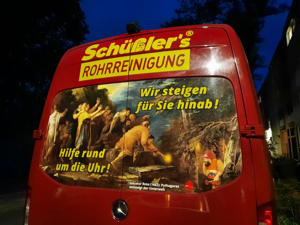 Das Heck von einem roten Transporter, Schüßlers Rohrreinigung. Ein Gemälde aus dem 17.Jahrhundert von Pythagoras, der aus der Unterwelt entsteigt, aller dings mit orangener Arbeitskleidung. Darauf der Text: wir steigen für sie hinab. Hilfe rund um die Uhr 