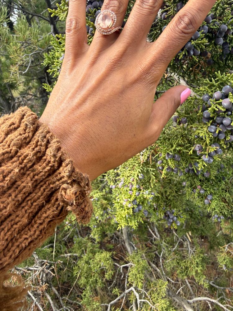 A woman’s hand with a spiral diamond and morganite engagement ring on her ring finger. 