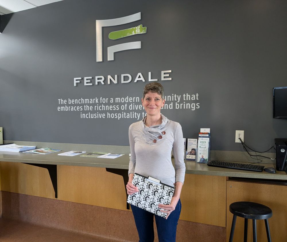 Quinn standing in the City Hall lobby, holding a file folder. Behind her is Ferndale's logo on the wall.