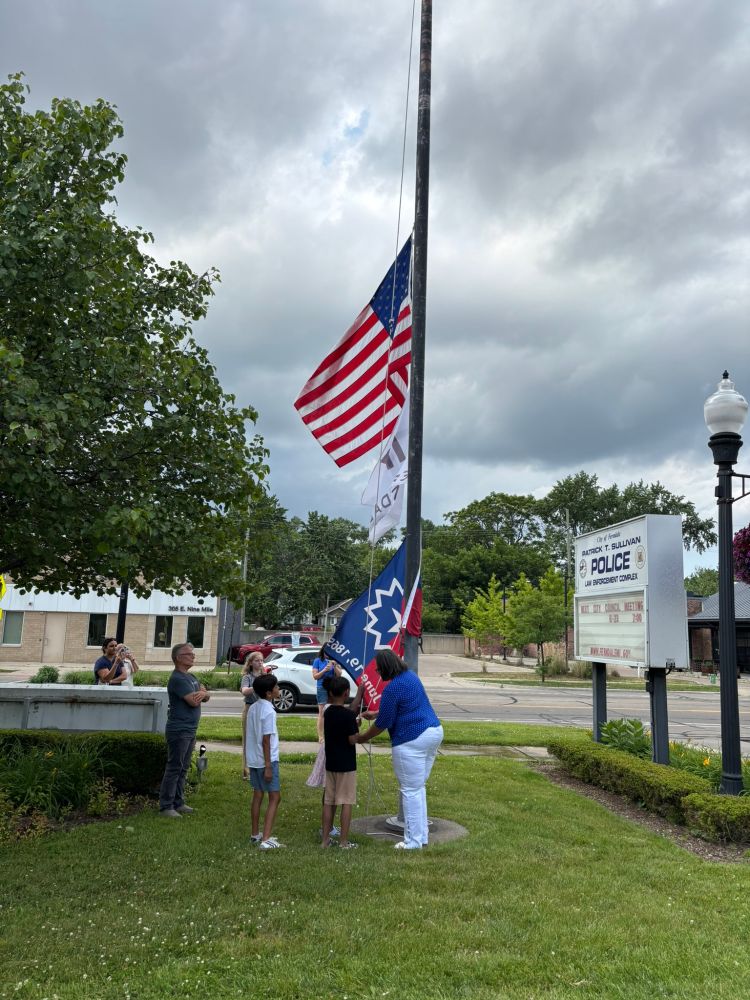 Mayor Raylon Leaks-May helps several children at a flagpole.