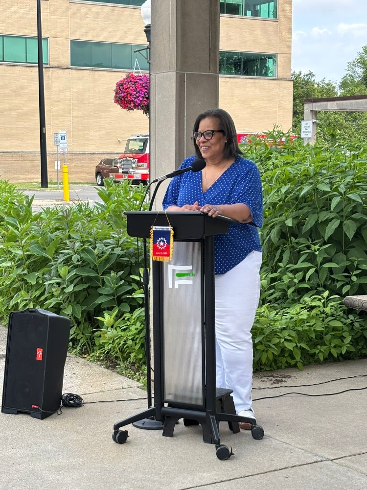 Mayor Raylon Leaks-May stands in front of a podium, smiling.