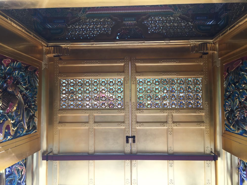 Gold doors with intricate window at top . Carvings on sides.
